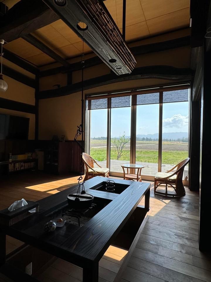 Full interior — irori table, rattan chairs, glass wall open to rice paddies